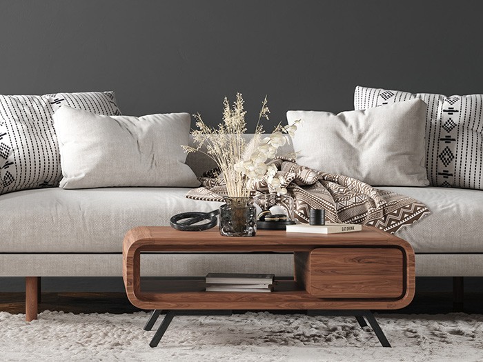 Light gray couch with rectangular decorative pillows and a Mid-century modern wooden coffee table on a white rug.